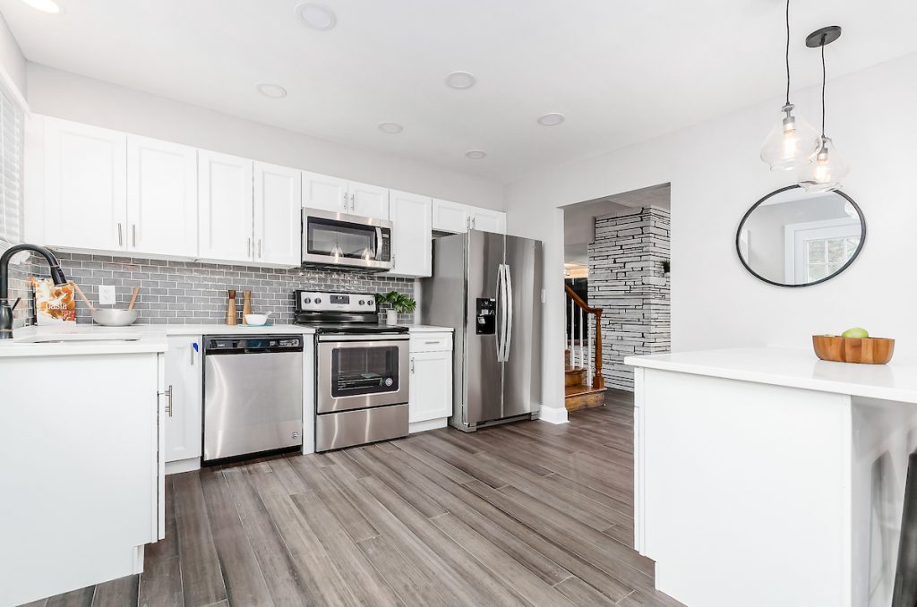 A kitchen with a small mirror, stainless steel appliances, and nice flooring.