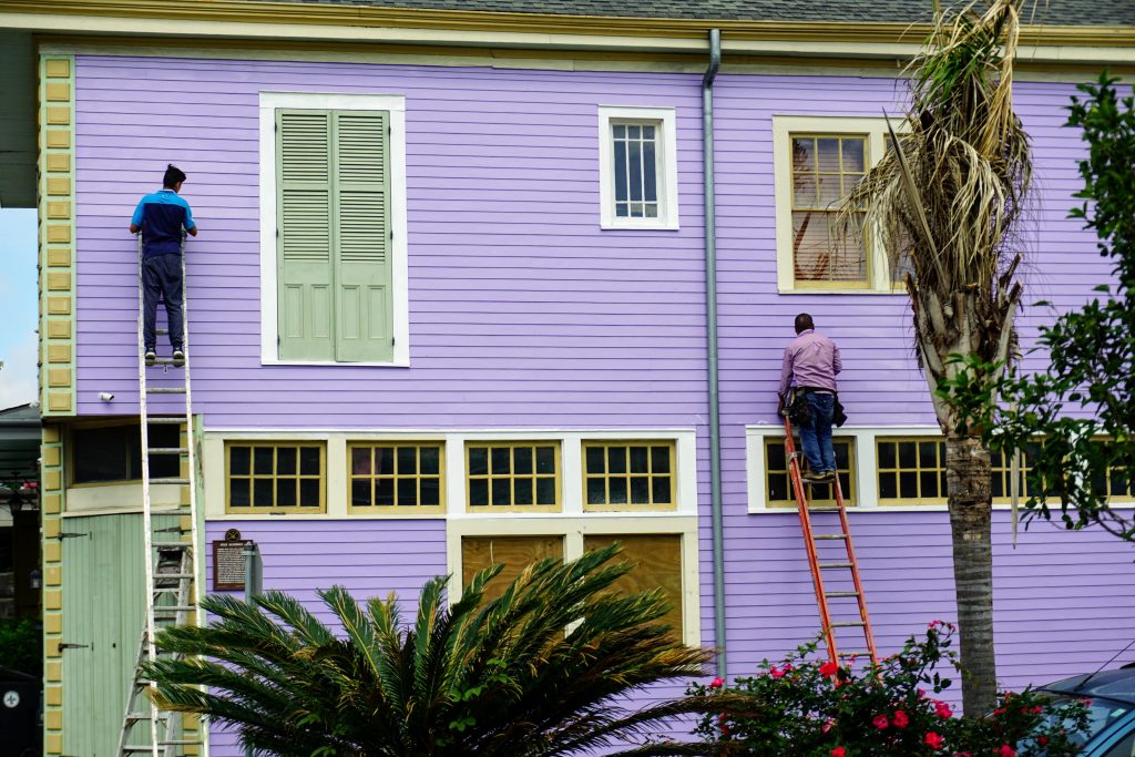 Two men on ladders painting the exterior of a purple building — one of the priciest home renovation costs there is. 