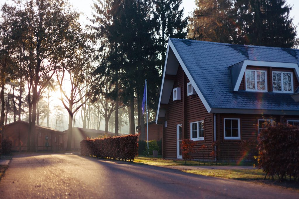 A beautiful home by a road surrounded by bushes and trees with a flag out front.