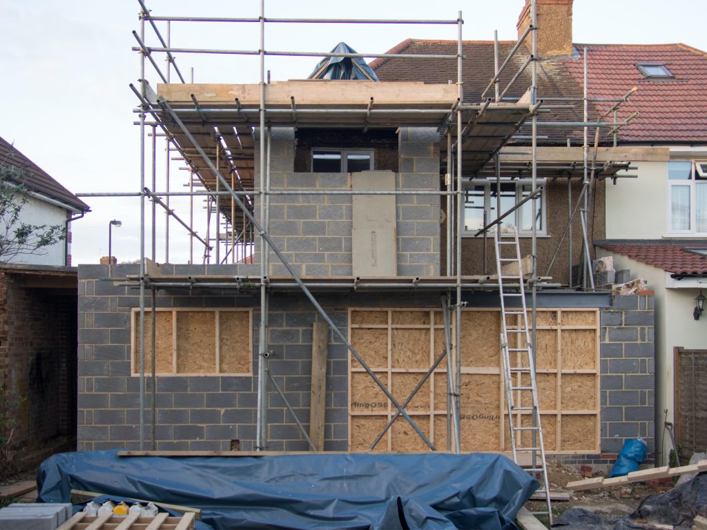 Scaffolding and a blue tarp around a a house that is being built.