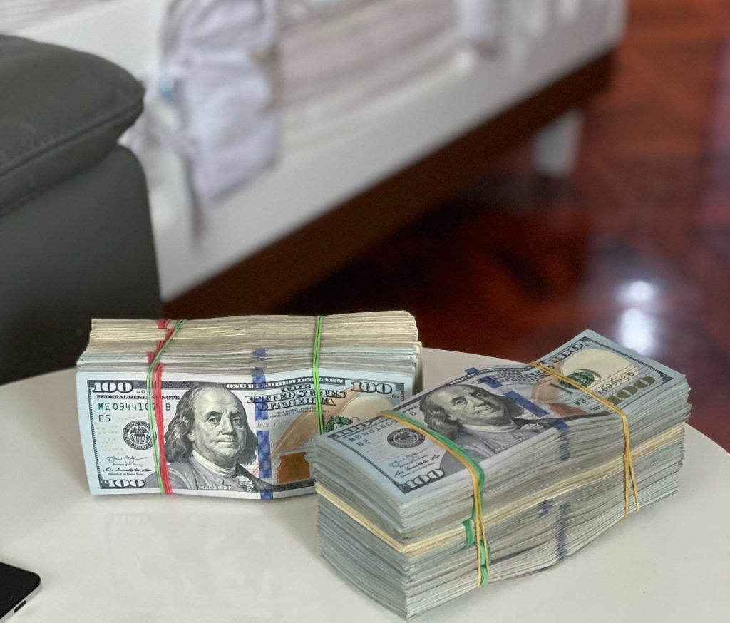 Two fat stacks of one-hundred-dollar bills on a table in a house.