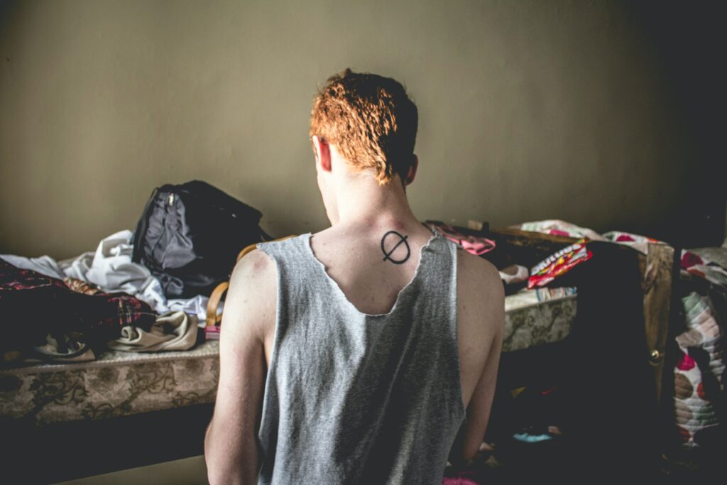 A redheaded male renter in front of an unruly bed.