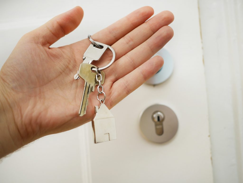 A hand holding a set of house keys with a house-shaped key ring attached.