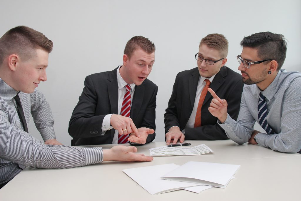 What does a title company do? It makes closing your home easier and safer as demonstrated by these four young men in business clothes and ties signing contracts on an eggshell white table.