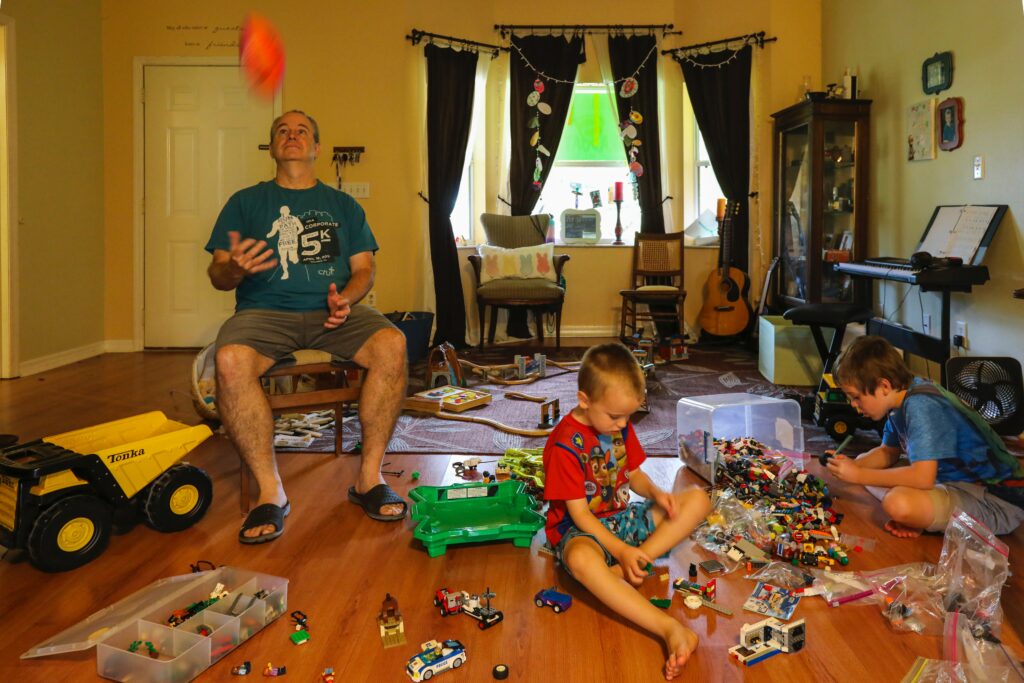 Two children and a man haven't learned how to prepare for a move as they sit playing with toys in a messy room.