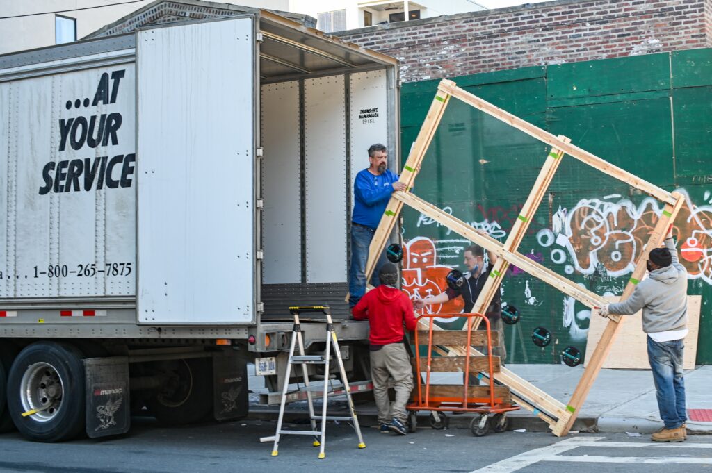 Four movers load a wooden bed frame onto a moving truck.