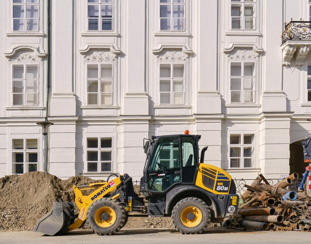 A yellow and black Komatsu bulldozer in front of an ornate off-white building.