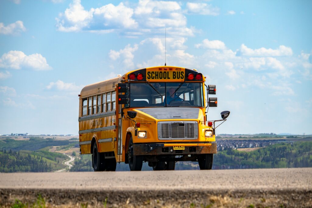 A school bus on the road under a blue sky and some fluffy clouds.