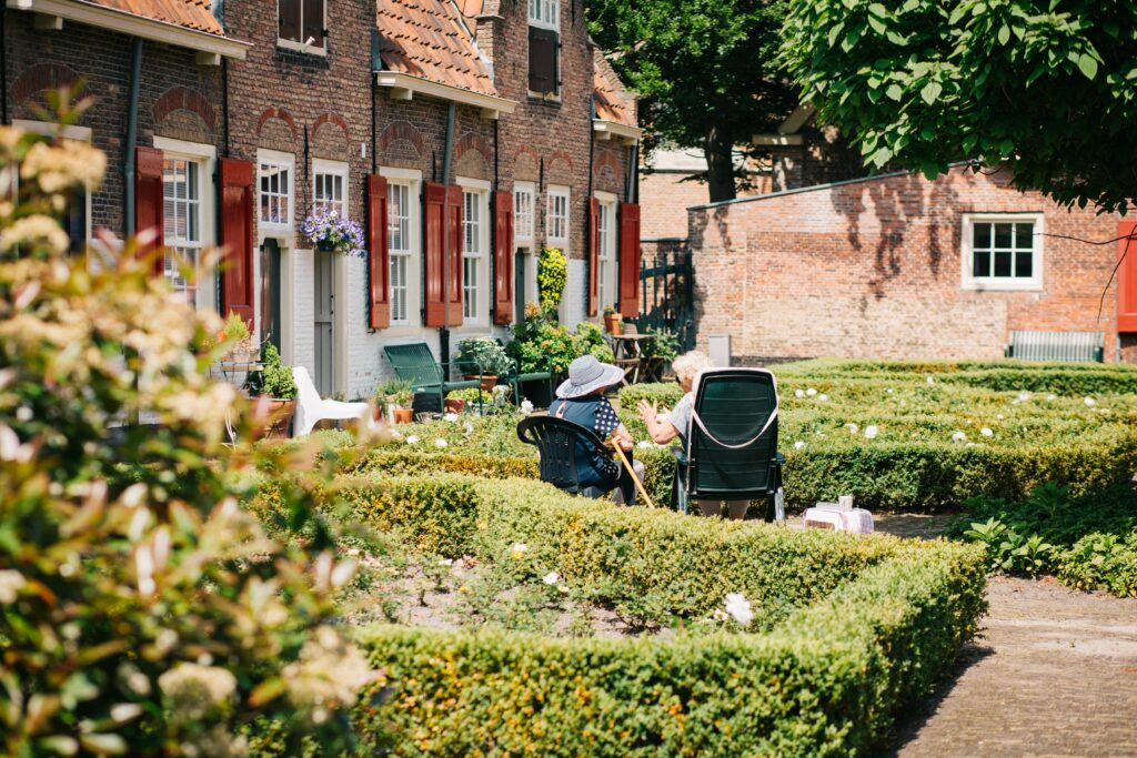 Two elderly folks sitting and chatting amongst shrubbery in a lovely outdoor area.