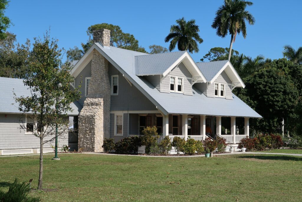 A muted blue home with grass out front and palm trees surrounding the property.