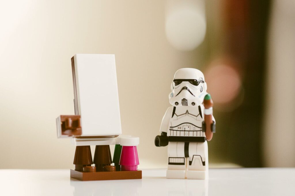 A LEGO Stormtrooper holding a paintbrush beside a toy easel.