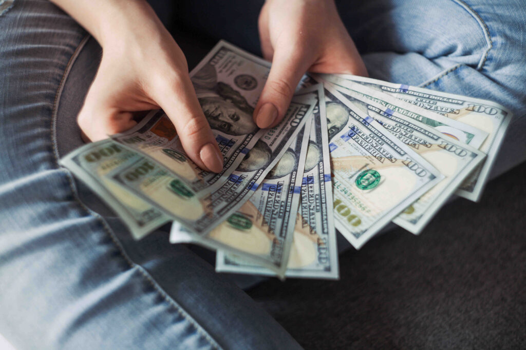 A person tallying up moving costs with a handful of one-hundred-dollar bills.