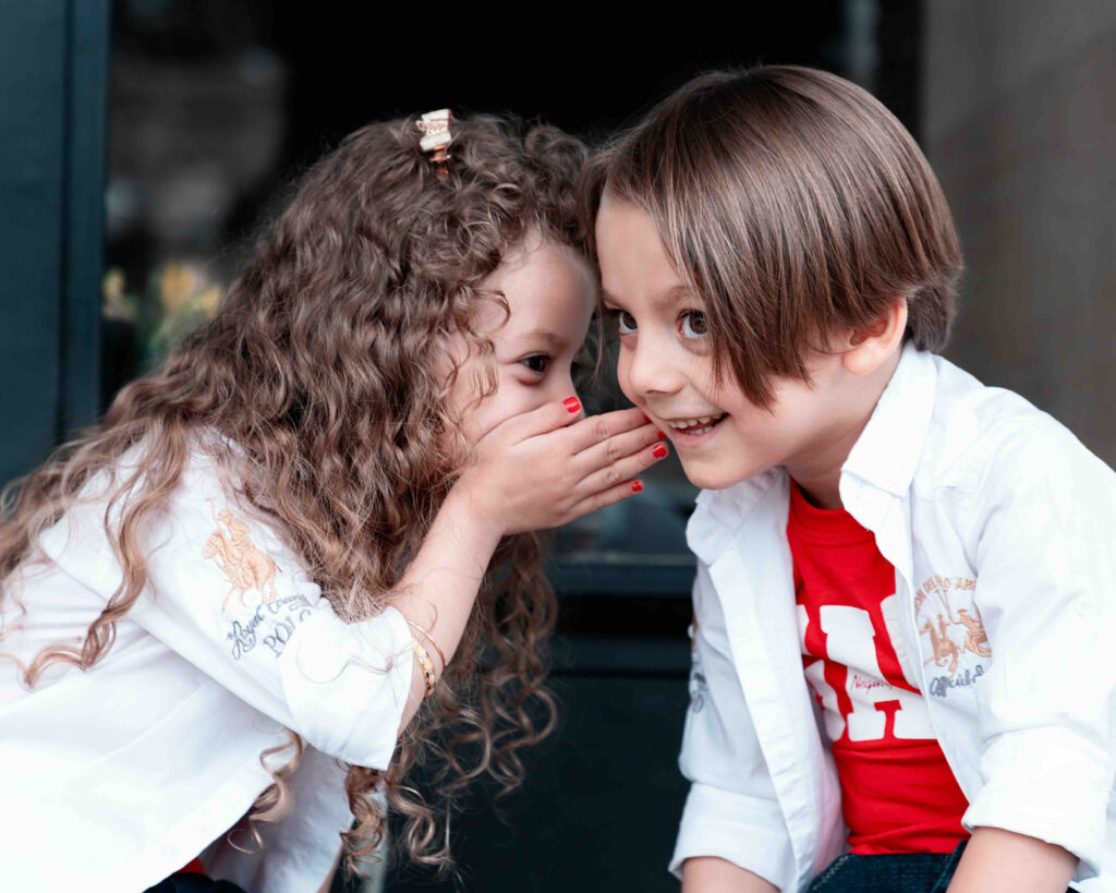 A little girl whispering a secret to a little boy.